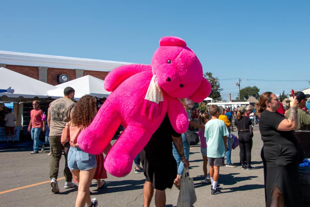 a giant pink teddy bear being carried outside on a clear day