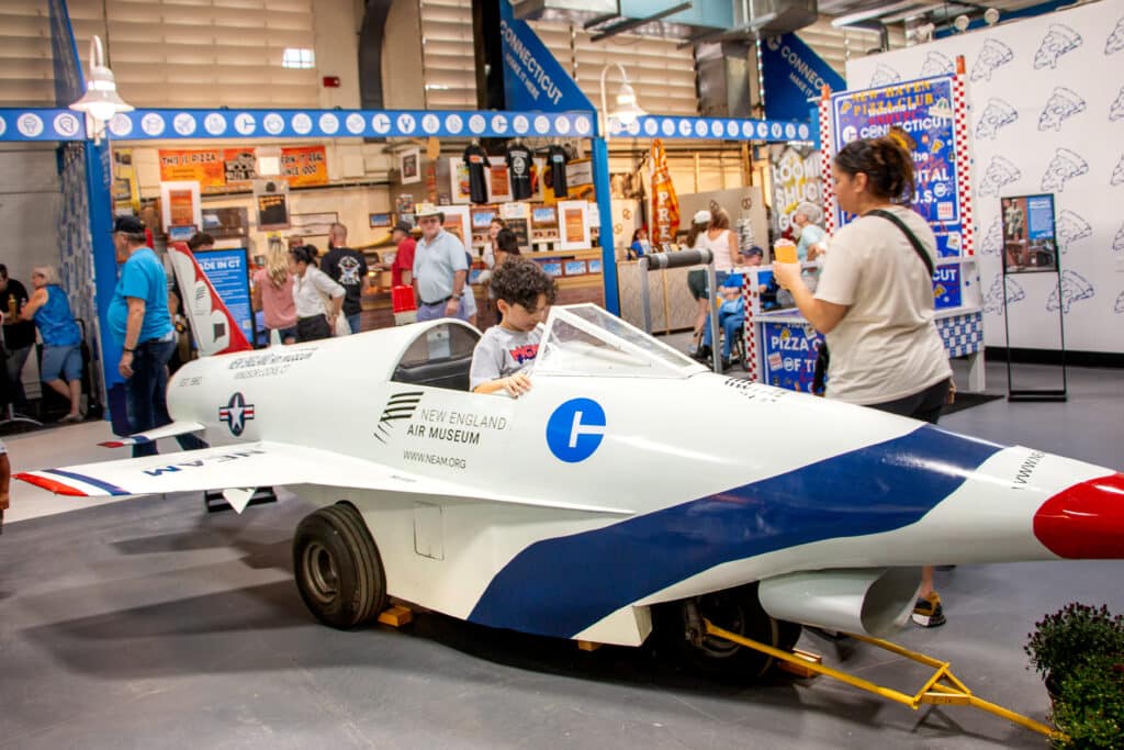 A boy sitting in a model airplane cockpit inside a building at the Big E