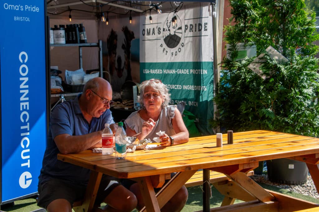 A man and a woman sitting at a picnic table eating fair food at the Big E